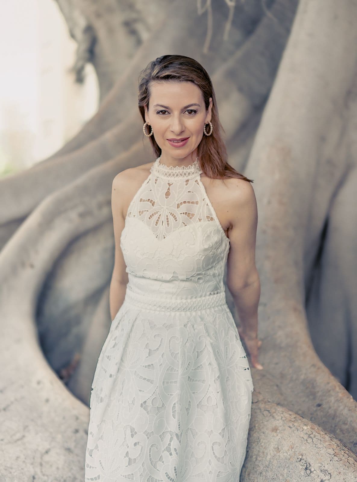 Chen Reiss in a white lace dress beneath the roots of a great tree