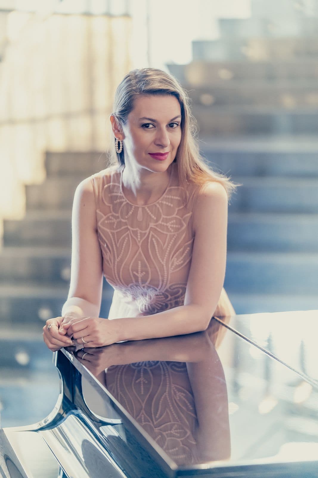 Chen Reiss leaning on a grand piano before a sunlit staircase