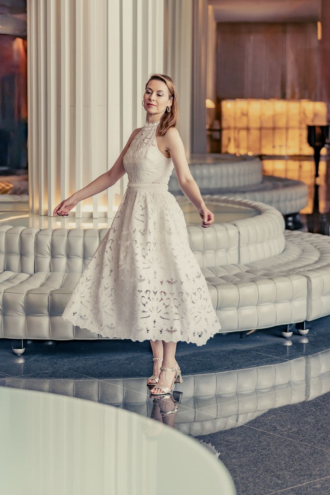 Chen Reiss in a white dress, mid-turn in a grand hotel lobby