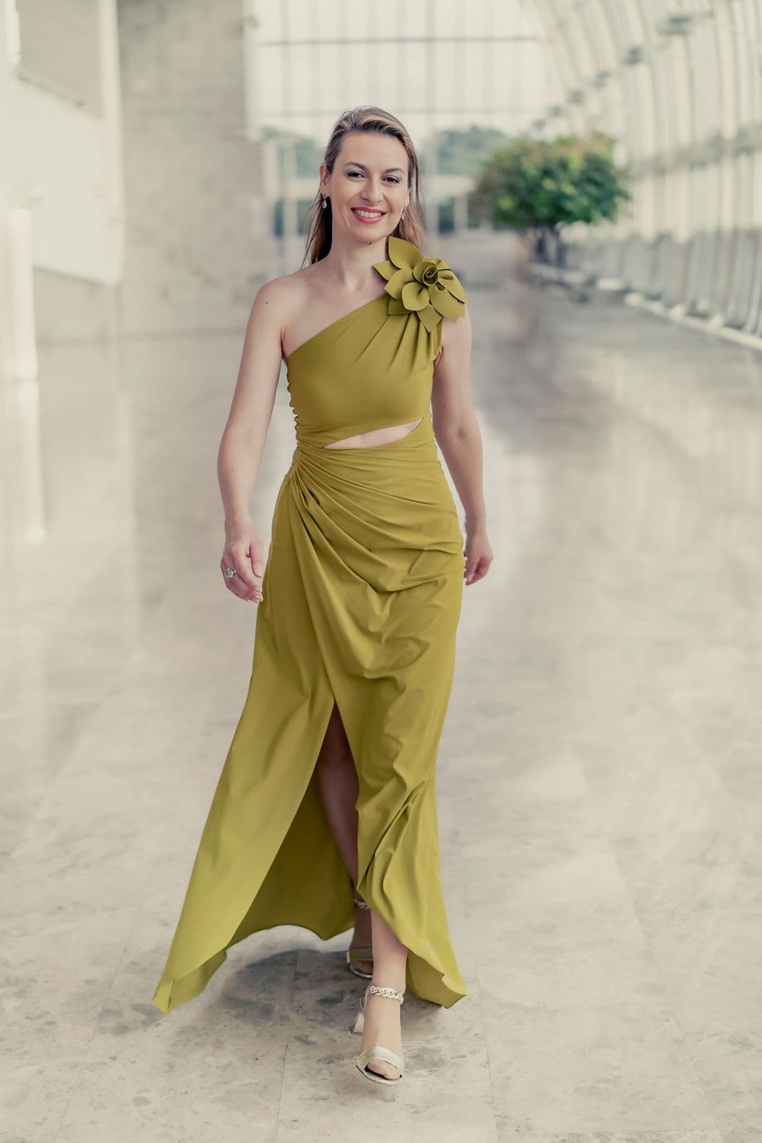 Chen Reiss walking through a bright gallery in an olive-gold gown